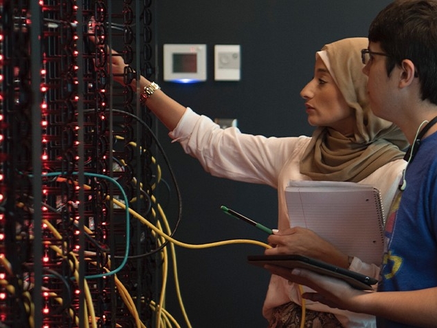 Cybersecurity students plug wires into a large, colorful, lit-up server