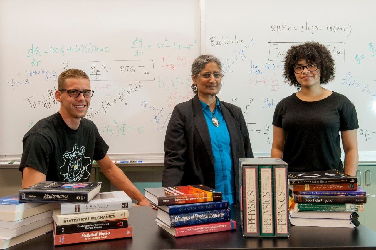 Physics students standing next to professor in classroom