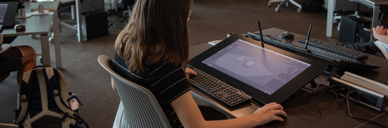 Student at a workstation, working on a 3D design on a tablet.