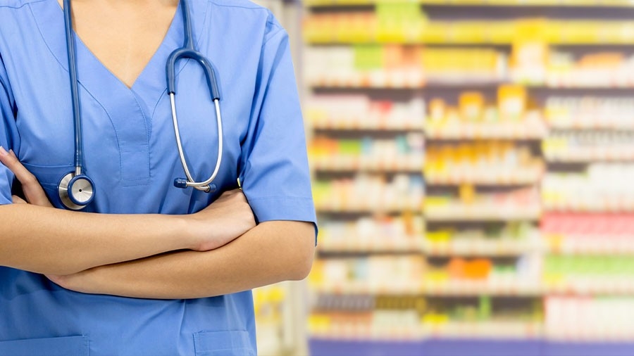 A technician stands with her arms folded in front of a shelf of medications